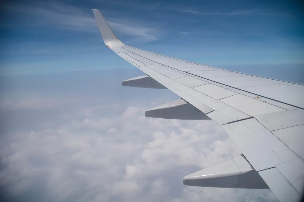 Plane wing up in the air with white clouds